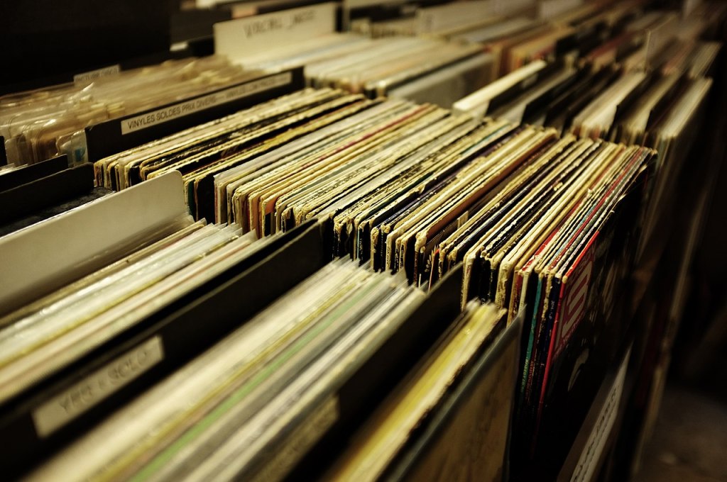 A picture of vinyl records all stacked in a collection at a record store.